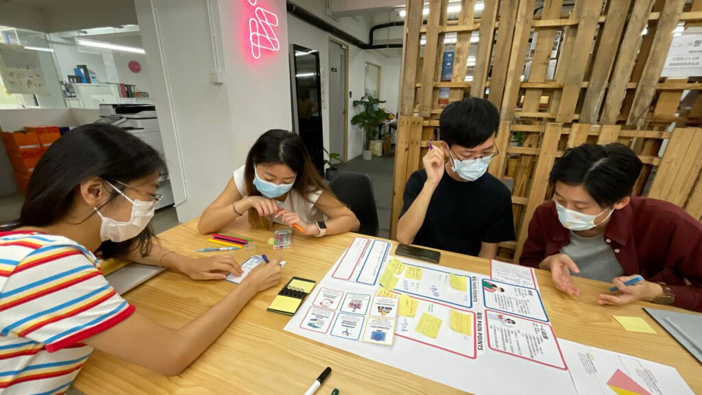 Four colleagues wearing masks, collaborating around a table decorated with colorful notes and charts on community legal education in a modern office setting.