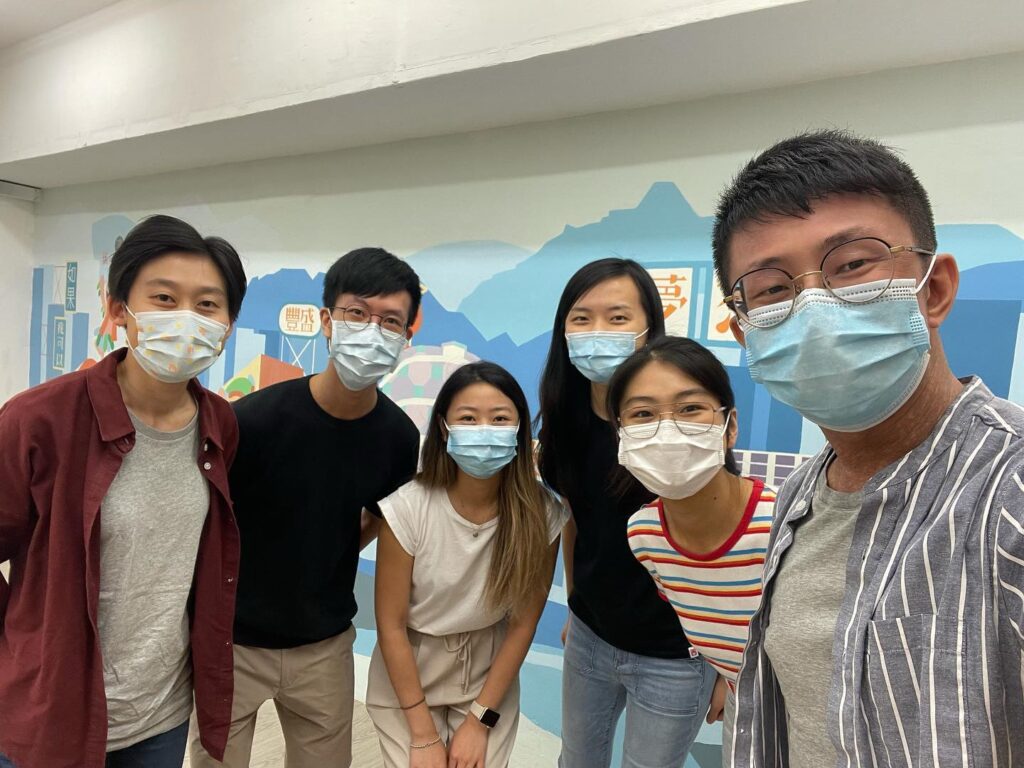 Group of six young adults wearing masks posing for a photo in a room with an educational mountain mural in the background.