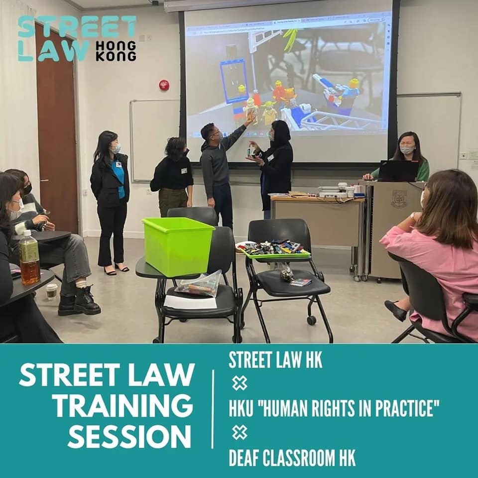 A classroom with seven attendees observing a presentation on human rights by three speakers, one using sign language, under the banner of "Community Legal Education.