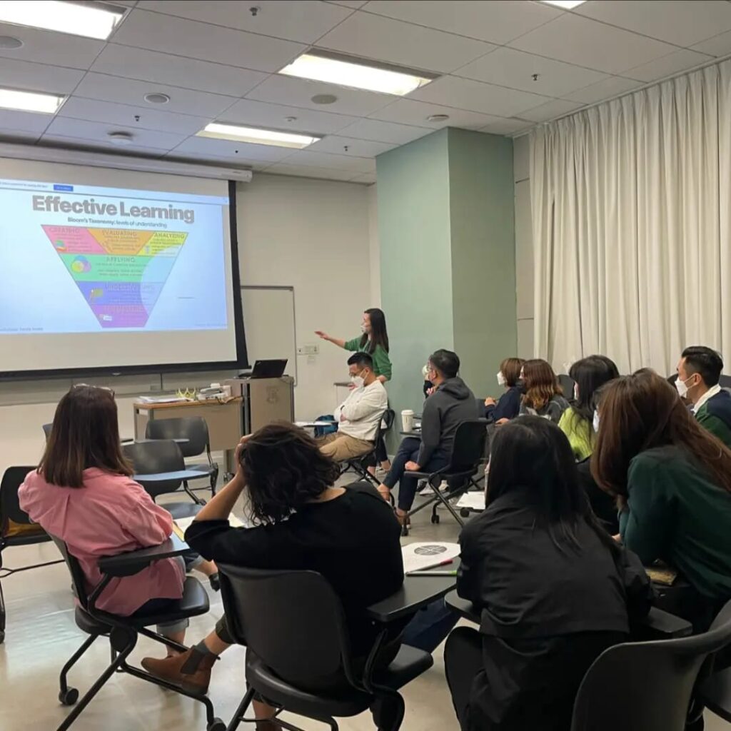 A professional presentation in a classroom with attendees looking at a slide titled "community legal education" projected on the screen, while a presenter gestures towards it.