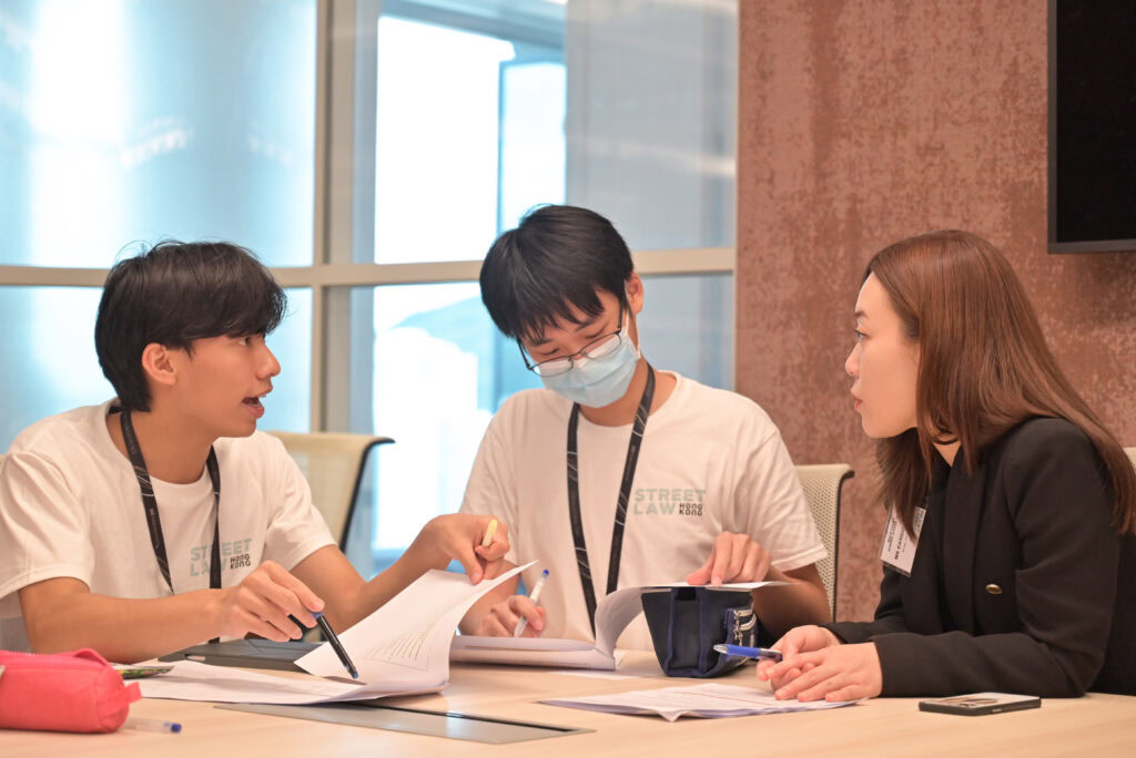 Three people, two men and a woman, engaging in an educational discussion over documents at a table in a well-lit room.