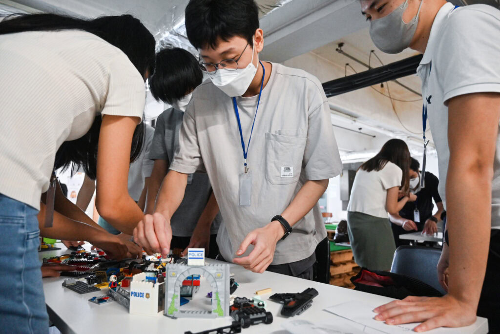 Group of children building lego models at a workshop, wearing masks and focused on assembling various pieces.