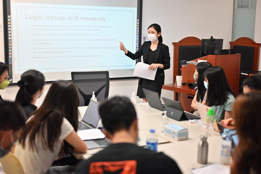 A female instructor in a mask discusses legal issues with university students in an education session.