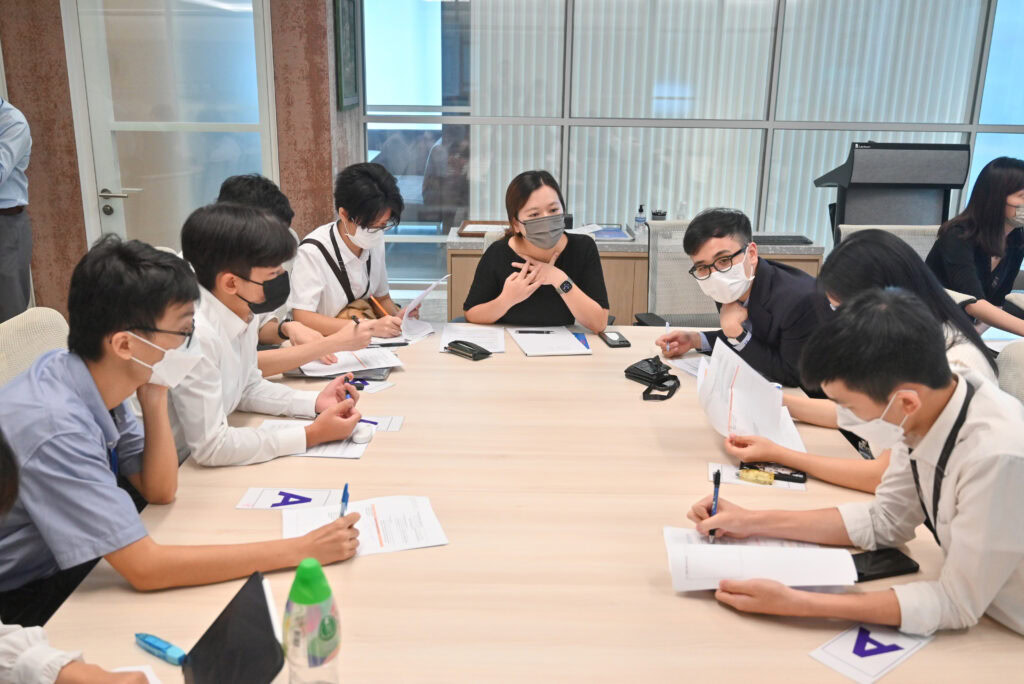 Group of masked business professionals engaged in a community legal education meeting around a table with documents and pens in hand.