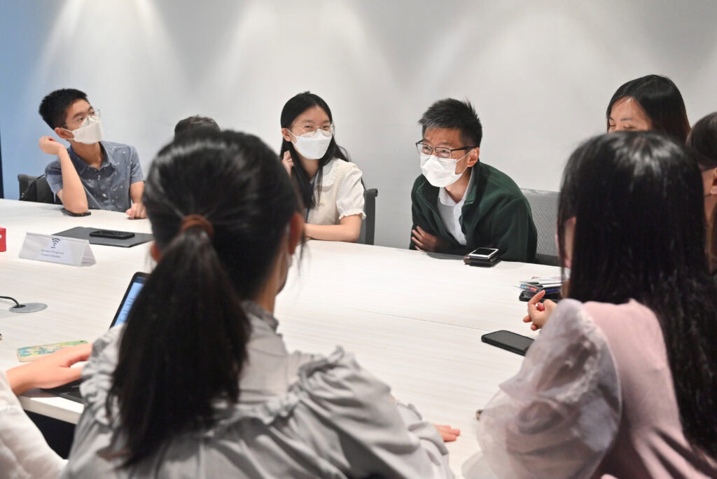 Group of young adults wearing masks, engaged in a discussion about accessible legal education around a conference table in a well-lit meeting room.