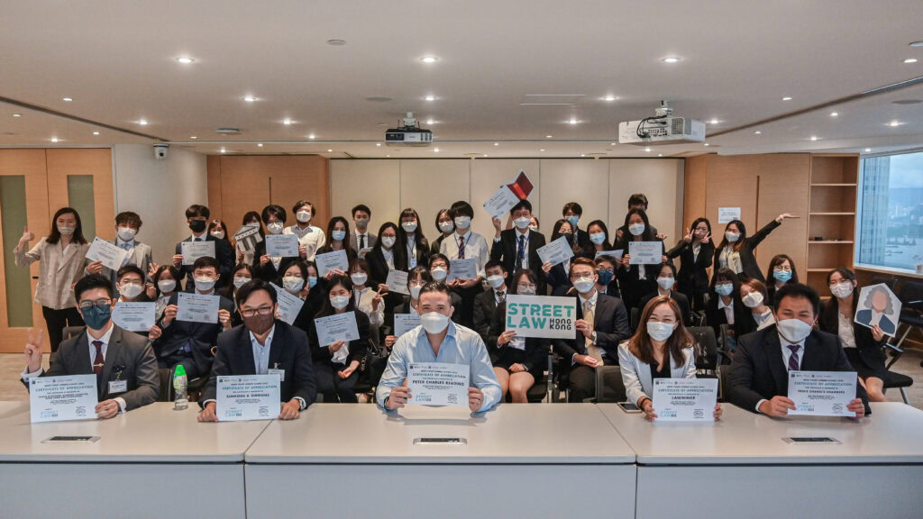 Group of individuals in business attire, wearing masks and holding certificates, seated in a conference room. Some are standing and waving, celebrating their continuing education achievements.