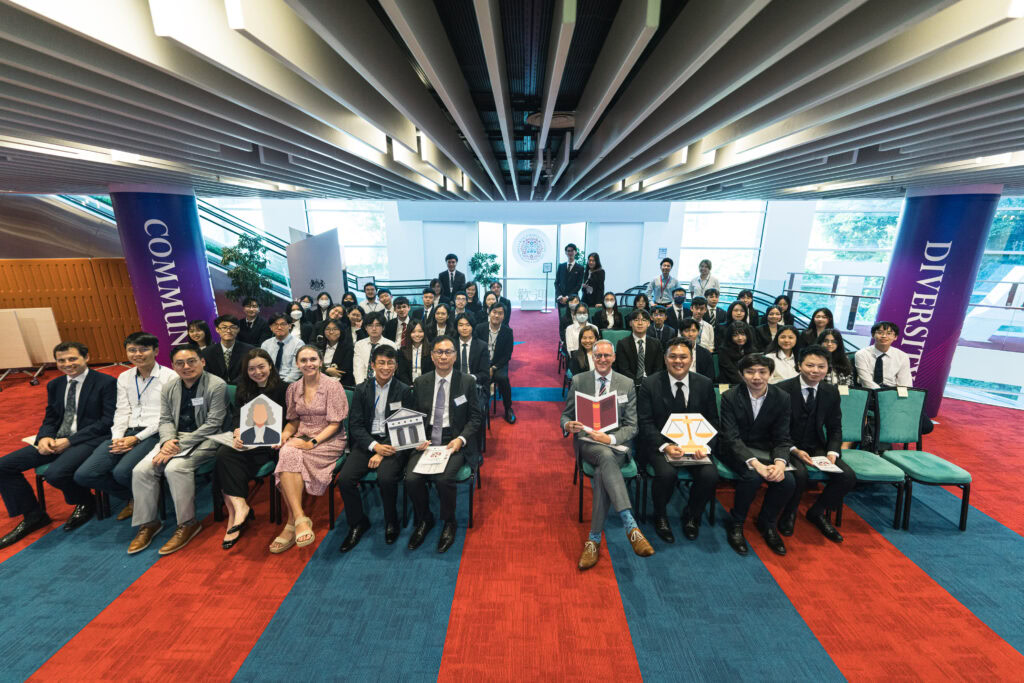 Group of legal professionals seated and standing in a conference hall, smiling at the camera, with banners reading "community" and "diversity.