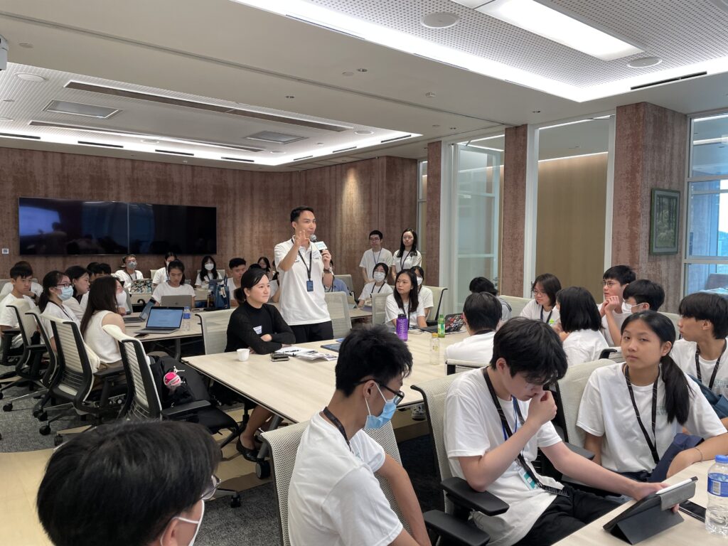 A large conference room with a man standing and speaking to a seated group of students, most using laptops, in an attentive legal education classroom setting.